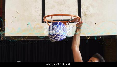 Der Athlet im Tank-Top schickt blauen Basketball durch das weiße Netz am orangefarbenen Rand an den Wellenformen des Fitnessstudios Stockfoto