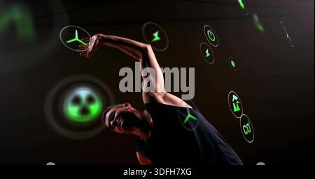 Ausladende Tänzerin in schwarzem Tank oben im Studio, mit leuchtender Windturbine und CO2-Symbolen Stockfoto