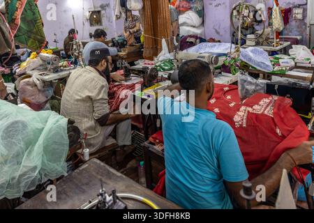 Fachkräfte, die auf Nähmaschinen in einer kleinen Bekleidungsfabrik in Delhi, Indien, sitzen und Nähstoffe nähen. Stockfoto