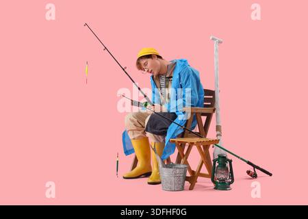 Lustiger junger Mann mit Angelrute, der im Stuhl auf rosa Hintergrund schläft Stockfoto