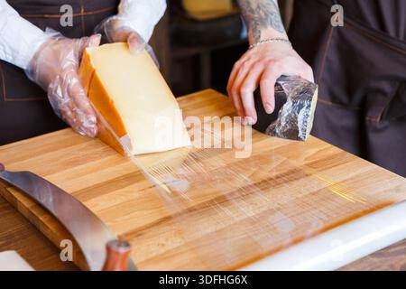 Der Ladenassistent wickelt ein Stück Käse ein Stockfoto