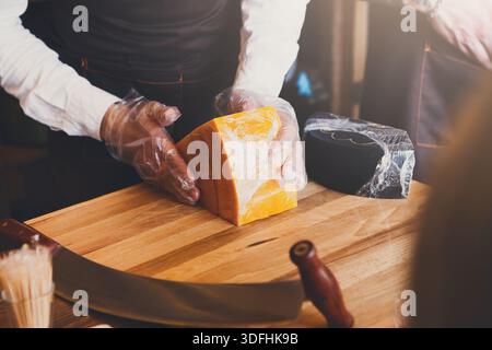 Der Ladenassistent wickelt ein Stück Käse an der Theke ein Stockfoto