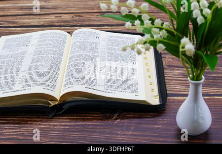 Öffne die Bibel mit Lily of the Valley auf Holztisch Stockfoto