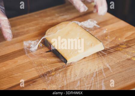 Der Ladenassistent wickelt ein Stück Käse ein Stockfoto