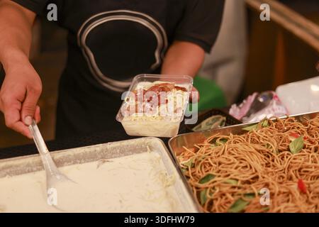 Ein Anbieter hält eine Plastikkiste voll mit leckeren Carbonara Spaghetti mit cremiger Sauce mit fröhlichem Gefühl, während er abends Essen zum Kunden bringt Stockfoto