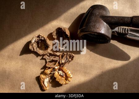 Eine rustikale Szene mit gerissenen Walnusshüllen und einem Nussknacker auf braunem Papier, mit natürlichen Texturen und warmer Beleuchtung Stockfoto