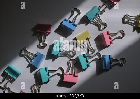 Eine Sammlung von bunten Binderclips, die auf einer Oberfläche verstreut sind und Schatten durch Sonnenlicht werfen Stockfoto