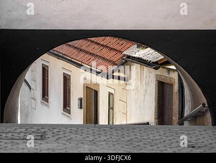 Blick durch einen bogenförmigen Durchgang in Skofja Loka zu einem rustikalen Gebäude mit rotem Dach. Stockfoto