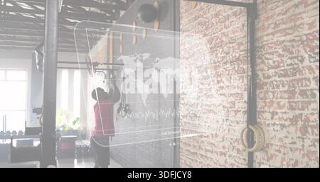 Der Athlet wird in rotem Tanktop und dunklen Shorts im industriellen Fitnessstudio erreicht, das Kletterpegboard mit Ringen Stockfoto