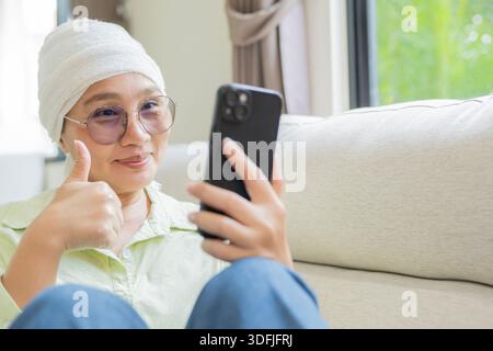 Glückliche reife asiatische Frau mit Brille nach Chemotherapie, die zu Hause auf dem Handy telefoniert. Kopierbereich. Stockfoto