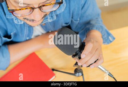Hochwinkelansicht eines bärtigen Mannes mit rotem Buch, das Mikrofon hält, während er zu Hause sitzt. Stockfoto