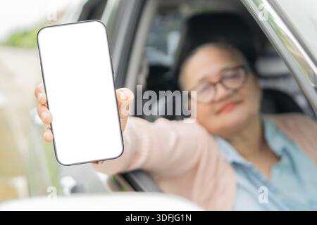 Ältere asiatische Frau mit Brille sitzt im Auto und zeigt einen Bildschirm mit Smartphone. Kopierbereich. Selektiver Fokus. Stockfoto