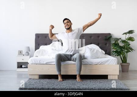 Ein glücklicher Araber wacht auf und dehnt sich im Bett, genießt einen frischen Morgen Stockfoto