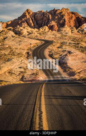 Blick auf eine gewundene Asphaltstraße, die durch die trockene, felsige Landschaft unter einem blauen Himmel führt und zu den majestätischen rötlich-braunen Bergen, Overton, Stockfoto