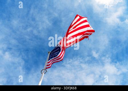 Tiefwinkelansicht der Nationalflagge der Vereinigten Staaten von Amerika, die auf einem Fahnenmast vor blauem Himmel winkt Stockfoto