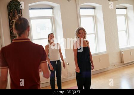 Yoga, Frau und glücklich mit Lehrer in der Klasse für Anweisungen, Übungstipps oder Wellness. Gruppe, weibliche Person und Coach mit Rat für ganzheitliche Stockfoto