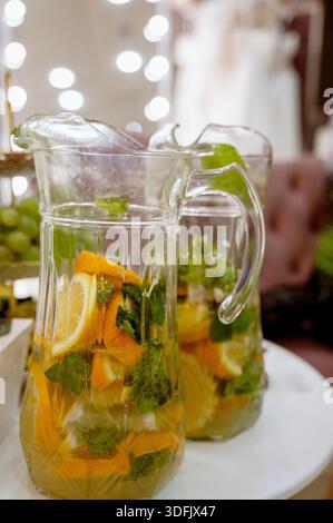 Ein Krug mit erfrischendem, fruchtigem Orangentee mit Eis und Minze. Zwei Krüge auf dem Tisch im Inneren. Trauben im Hintergrund. Sommer erfrischend dr Stockfoto
