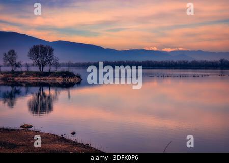 Kerkini, Nordgriechenland – das Licht bei Sonnenuntergang überflutet schneebedeckte Gipfel und ruhige Reflektionen des Sees und schafft eine ruhige und harmonische Landschaft. Stockfoto