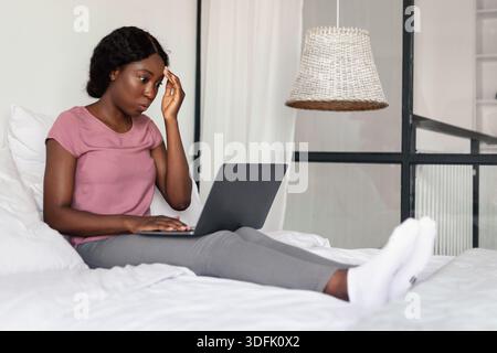Aufgeregte Schwarze Frau Mit Laptop-Computer, Die Internet Im Schlafzimmer Surft Stockfoto