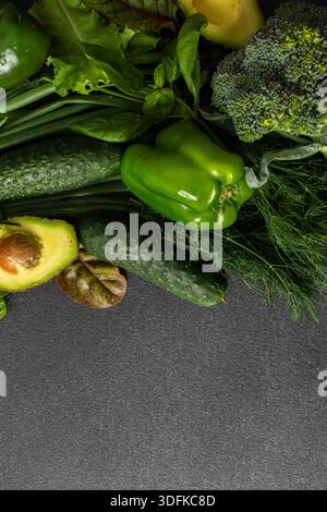 Eine Vielzahl von frischem, grünem Gemüse ist ordentlich auf einer dunklen Oberfläche angeordnet und zeigt Gurken, Paprika, Avocado, Brokkoli, und verschiedene Blattgemüse, gesunde Ernährung für einen nahrhaften Salat Stockfoto