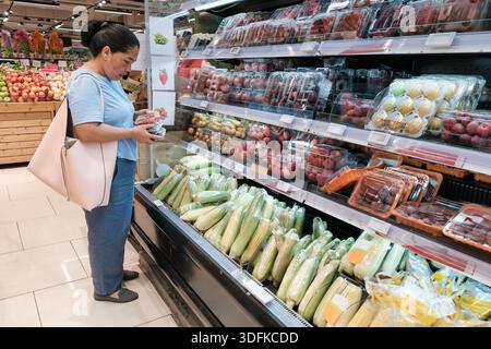 Eine Frau wählt frisches Gemüse und Obst in einem Supermarkt aus. Sie steht vor Regalen, in denen verschiedene Artikel ausgestellt sind. Stockfoto