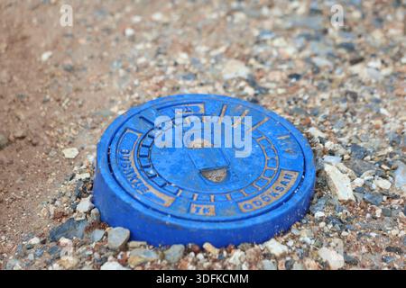 Blaue Abdeckung des unterirdischen Wassernetzes auf Kies für den Zugang zur städtischen Infrastruktur Stockfoto