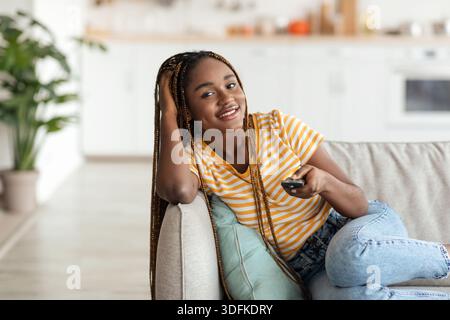 Entspannte junge afroamerikanische Frau, die zu Hause fernsieht Stockfoto