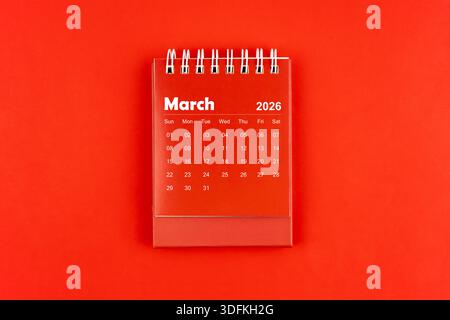 März 2026 roter Schreibtischkalender auf rotem Hintergrund, Flat Lay. Stockfoto