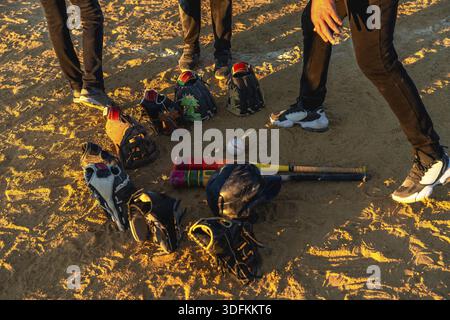 Baseballspieler versammeln sich bei Sonnenuntergang auf einem staubigen Feld und diskutieren ihre Strategie, während ihre Fledermäuse, Helme und Handschuhe auf dem Boden liegen und sich auf eine Ga vorbereiten Stockfoto