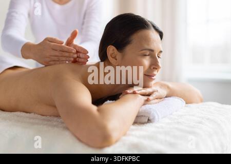 Erwachsene Frau, die sich während der Spa-Massage friedlich ausruhen, Kopf auf gefaltetem Handtuch Stockfoto