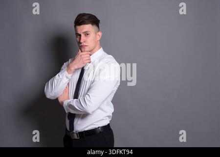Selbstbewusster junger Mann posiert nachdenklich in einem neutralen Studio-Setting Stockfoto