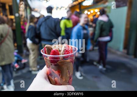 Hand hält frische Erdbeeren mit geschmolzener Schokolade auf dem Markt Stockfoto