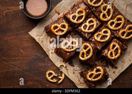 Schokoladen-Brownies mit Nüssen, gesalzenem Karamell und Brezeln, Blick von oben, hölzerner Hintergrund Stockfoto