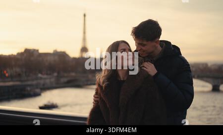 Ein romantisches Paar umarmt den Eiffelturm im Hintergrund in Paris Frankreich bei Sonnenuntergang. Dieses Bild kann für Valentinstag- oder Flitterwochenkonzepte verwendet werden. || Modell freigegeben Stockfoto