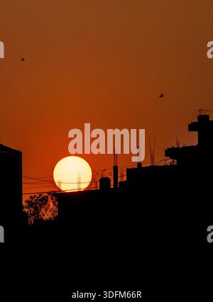 Ein atemberaubender Sonnenuntergang mit einer großen, leuchtend gelben Sonne, die unter den Horizont fällt. Der Himmel ist in warmen Orangen-, Gold- und Weichstiften gemalt Stockfoto