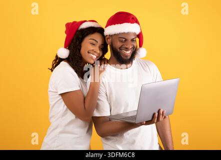 Saisonale Verkäufe. Glückliches afroamerikanisches Paar, das auf Laptop-Computer schaut und lächelt, auf gelbem Hintergrund stehend Stockfoto