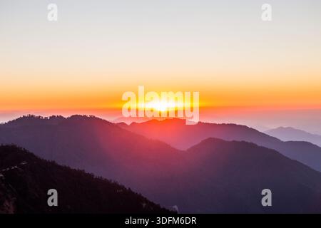 Ein atemberaubender Sonnenuntergang mit einer großen, leuchtend gelben Sonne, die unter den Horizont fällt. Der Himmel ist in warmen Orangen-, Gold- und Weichstiften gemalt Stockfoto