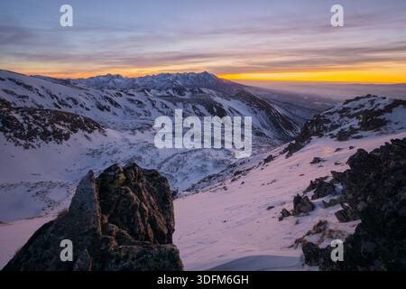 Blick auf die schneebedeckten Berge bei Sonnenuntergang, im Kontrast zu den dunklen, zerklüfteten Felsen im Vordergrund, Nizna Bystra, Region Zilina, Slowakei. Stockfoto
