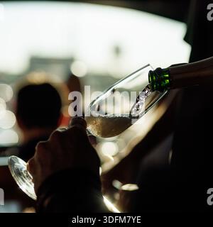 Nahaufnahme des Sekts, der während einer Sonnenuntergang-Versammlung in ein Glas gegossen wird. Die Szene zeigt Hände, die die Brille halten, mit warmem und weichem Licht Stockfoto