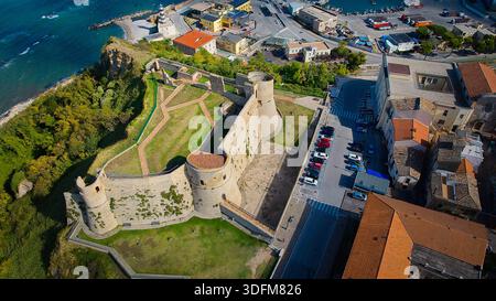 Luftbild mit dem Castello Aragonese, das dramatisch auf einer Klippe am Meer thront, mit ruhigem türkisfarbenem Wasser unter und klarem Himmel, der den Hist beleuchtet Stockfoto