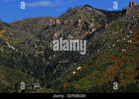 Felsige Hügel mit Herbststräuchern ragen über ein Haus im Tal und Kiefern, vom Pikes Peak Highway in der Nähe von Colorado Springs, Colorado, USA. Stockfoto
