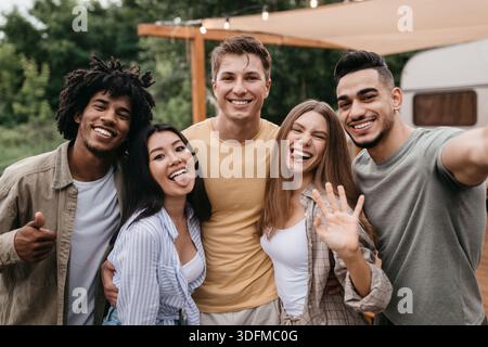 Glückliche, vielfältige junge Freunde posieren in der Nähe von Wohnmobil, Spaß haben, albern sein, zeigen verschiedene Gesten auf Campingausflug Stockfoto