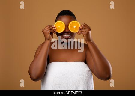 Plus Größe schwarze Frau, die die Augen mit Hälften von Orange bedeckt Stockfoto