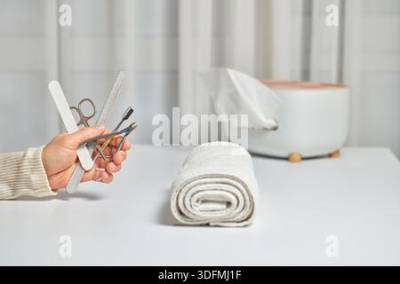 Person, die einen Satz Nagelpflegeinstrumente mit einem Handtuch und einer Taschentücherkassette in der Nähe hält Stockfoto