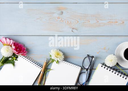 Notizbuch mit offener leerer Seite, Brille, Stift, weißer Tasse mit schwarzem Kaffee, Dahlienblüten. Kaffeetasse am Morgen. Stockfoto