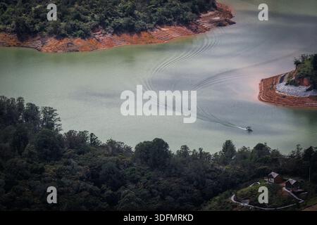 Blick auf ein Boot, das durch das ruhige, blassgrüne Wasser gleitet und Wanderwege vor dem Hintergrund der grünen Hügel, Peniol-Guatape Reservoir, Guata hinterlässt Stockfoto