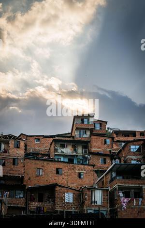 Blick auf Ziegelhäuser, die auf einem Hügel unter einem dramatischen Himmel gestapelt sind, Sonnenlicht durchdringt die Wolken und erzeugt einen starken Kontrast von Licht und Schatten. Stockfoto