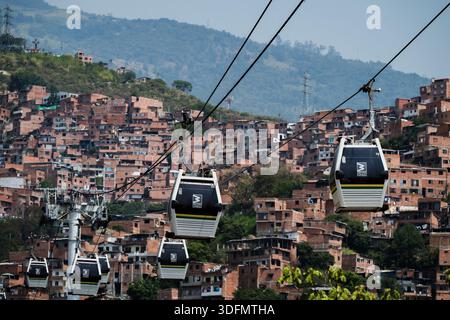 Blick auf die Seilbahnen gleiten über eine weitläufige Hangfavela, ein Wandteppich aus Ziegelhäusern, die in Richtung der üppig grünen Berge in Medellin, Kolumbien, klettern. Stockfoto