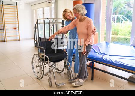 Ein Physiotherapeut hilft einer älteren Frau mit Rollstuhl in einem Reha-Zentrum mit Schwerpunkt auf Mobilität und Erholung. Dieses Bild kann kommerziell verwendet werden Stockfoto