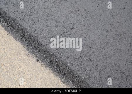 Frischer Asphalt trifft bei der Straßenerneuerung auf alten Beton, wodurch ein kontrastierender Hintergrund entsteht. Stockfoto